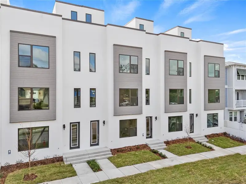 Modern white townhouses with large windows and green lawns.