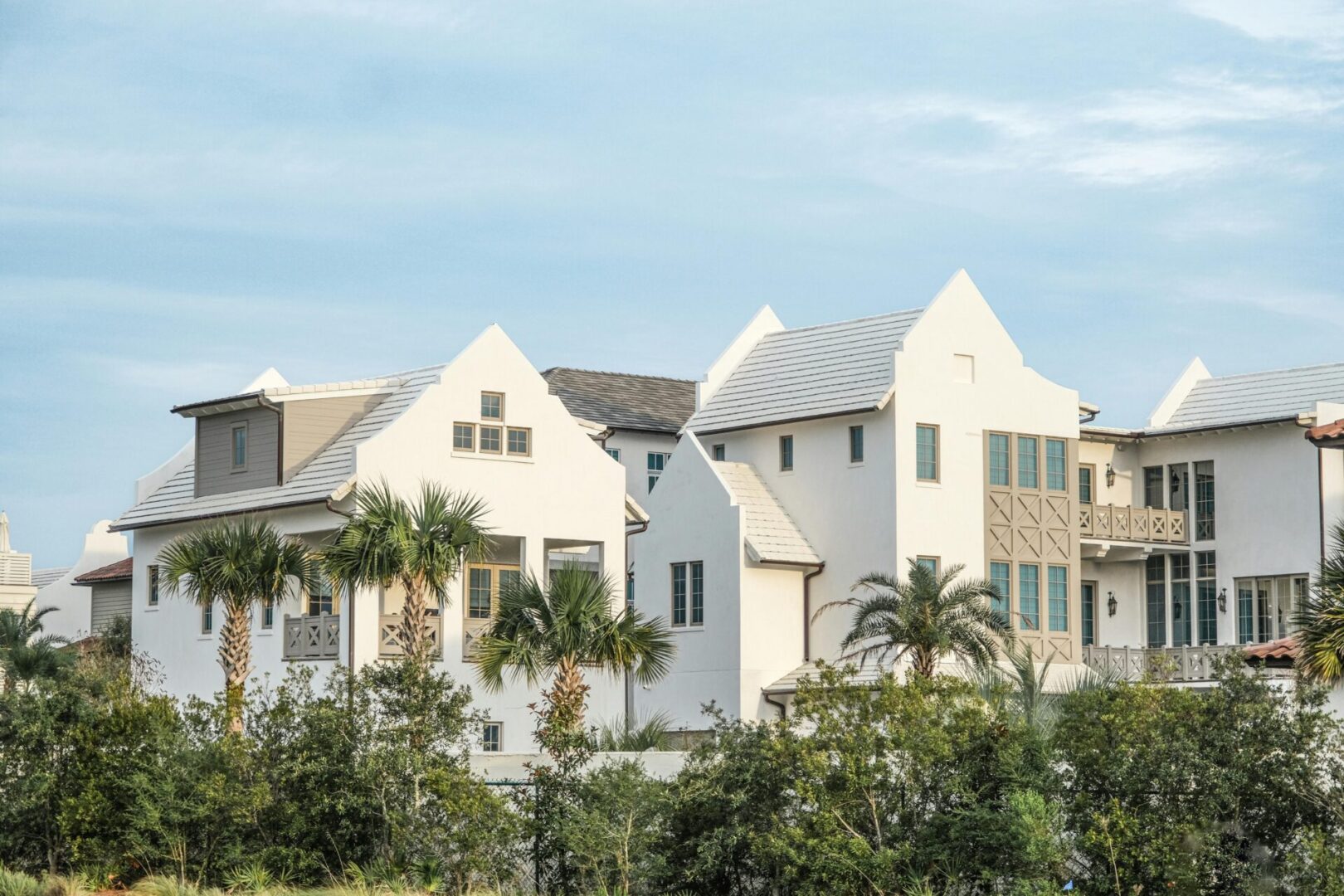 White modern houses with gable roofs and palm trees.